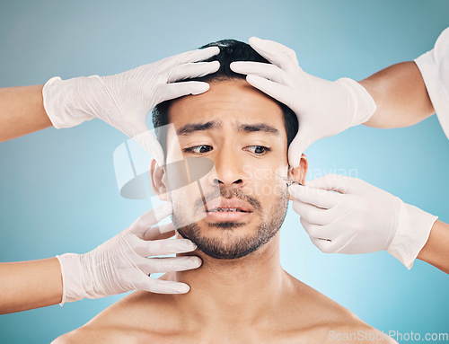 Image of Face, hands and plastic surgery with a worried man in studio on a blue background for beauty enhancement. Aesthetic, botox or change with a young male patient looking nervous in a clinic for skincare