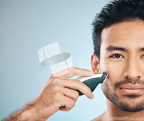 Image of Portrait, shaving and electric razor with a man in studio on a blue background for personal hygiene or grooming. Face, wellness and cosmetics with a young male in the bathroom for hair removal