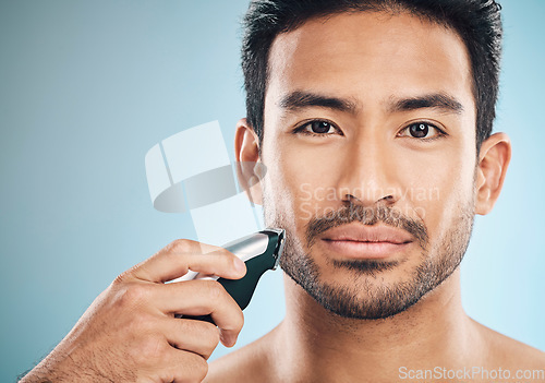 Image of Portrait, shave and electric razor with a man in studio on a blue background for personal hygiene or grooming. Face, wellness or cosmetics with a confident young male in the bathroom for hair removal