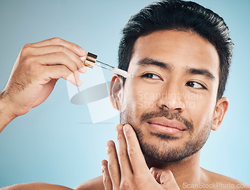 Image of Face, beauty and antiaging oil with a man in studio on a blue background for skincare or grooming. Luxury, serum or wellness with a handsome male person in the bathroom to apply a product to his face