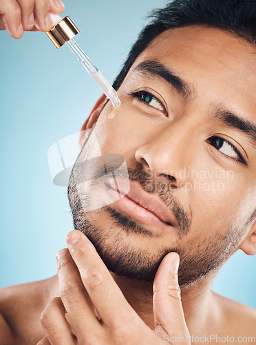 Image of Face, skincare and antiaging serum with a man in studio on a blue background for beauty or grooming. Luxury, oil or wellness with a handsome young person in a bathroom to apply a product to his face