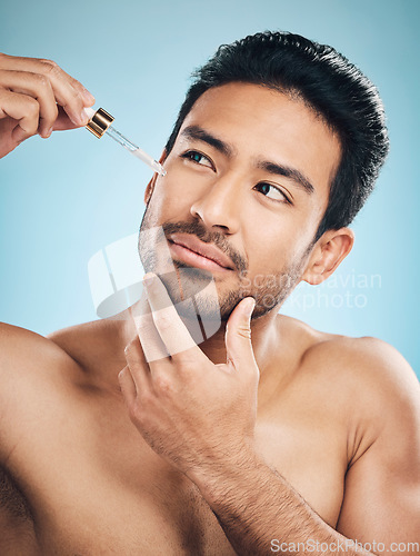 Image of Face, beauty and antiaging serum with a man in studio on a blue background for skincare or grooming. Luxury, oil or wellness with a handsome male person in the bathroom to apply a product to his skin