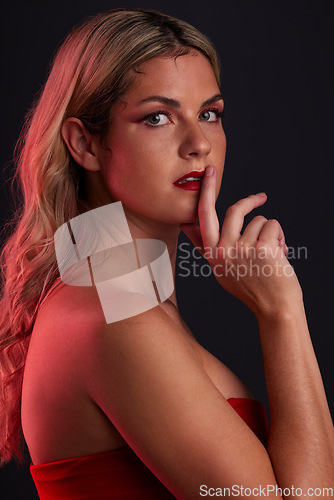 Image of Portrait, beauty and sensual with a model woman in studio on a dark background in red lighting for desire. Face, makeup or lipstick with a young female person posing for natural feminine confidence