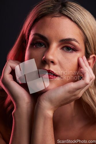 Image of Portrait, skincare and luxury with a model woman in studio on a dark background in red lighting for desire. Face, beauty and makeup with a young female person posing for natural feminine confidence