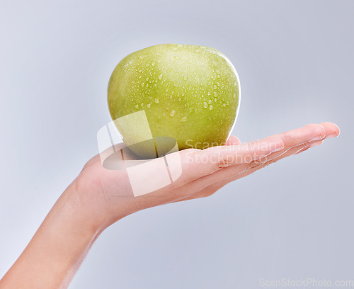 Image of Vegan, hand and apple with water drops, nutrition and clean against a grey studio background. Zoom, fingers and person with a fruit in a palm, detox and snack for diet with self care and wellness