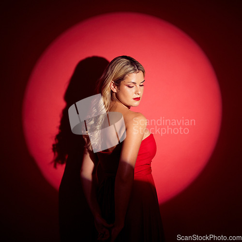 Image of Beauty, spotlight and red with a model woman in studio on a dark background for classy elegance or style. Fashion, aesthetic and luxury with a confident young female person standing in a dress