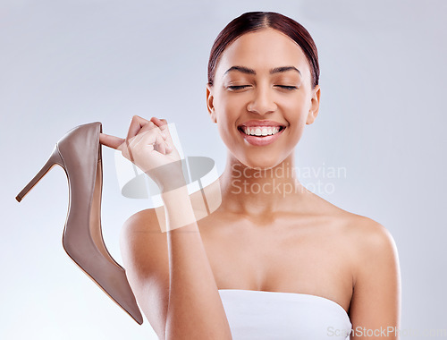 Image of Fashion, smile and high heel with a model woman in studio on a gray background for footwear advertising. Marketing, luxury or shopping with a happy young female customer holding a shoe for style