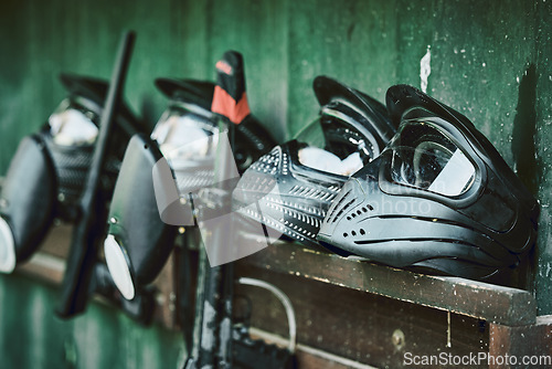 Image of Paintball, helmet and guns on rack at battle station of sports gear waiting for players, competition or war. Paint balling sportswear or stationary equipment ready for serious game, fight or warfare