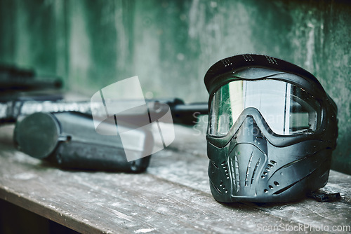 Image of Paintball, helmet and gun on table at battle station of sports gear waiting for player, competition or war. Paint balling sportswear or stationary equipment ready for serious game, fight or warfare