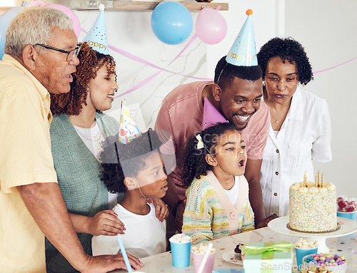 Image of Birthday, cake and a girl blowing out candles while celebrating with her black family in their home. Kids, party or celebration with parents, grandparents and children bonding together in a house