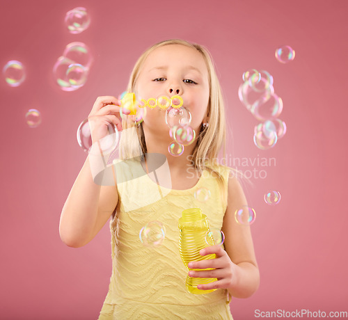 Image of Portrait, fun and girl blowing bubbles, content and playing in studio while posing against pink background. Hand, face and child enjoying freedom, toy and innocent magic while standing isolated