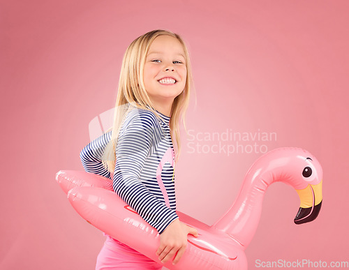 Image of Happy, portrait and pool float with girl in studio for swimming, summer break or cute. Youth, funny and inflatable with child and flamingo ring for relax, smile or beach holiday on pink background