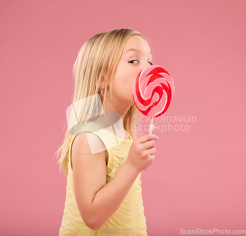 Image of Candy, sweets and lollipop with girl in studio for sugar, party and carnival food isolated on pink background. Cute, positive and youth with child and eating colorful snack for playful and treats