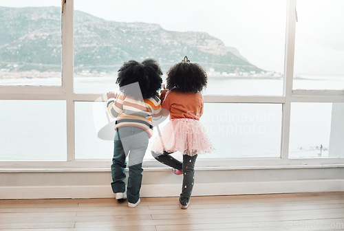 Image of View, back and children looking from a window for play, beach and childhood together. Indoors, standing and kids waiting in a house to visit the sea on a vacation or holiday at the ocean for playing