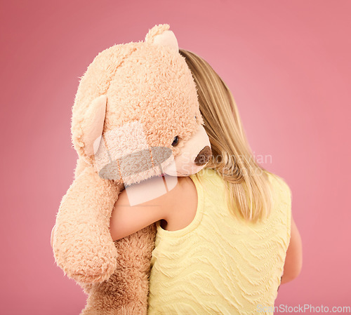 Image of Teddy bear, love and back of a girl in a studio with a big, fluffy and cute toy as a gift or present. Adorable, innocent and young child hugging her teddy with care and happiness by a pink background