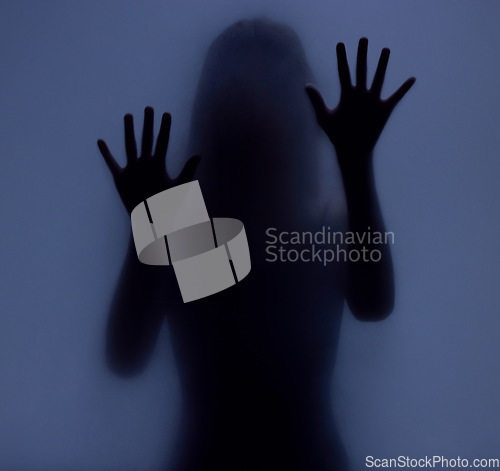 Image of Shadow, glass and hands with a woman in studio on a blue background for mystery or sensual secrecy. Creative, silhouette and window with a female posing for beauty, art deco or feminine desire