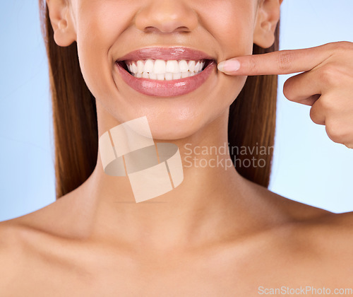 Image of Dental, pointing and teeth with smile of woman in studio for beauty, clean and self care. Oral hygiene, natural and cosmetic treatment with girl model on blue background for veneers, fresh or results