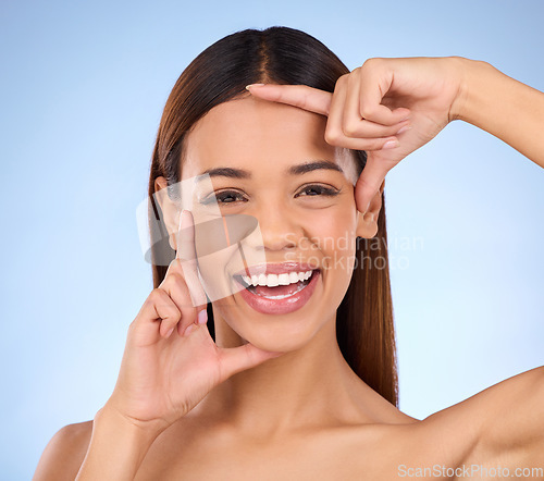 Image of Woman, beauty and hands on face portrait for skincare dermatology cosmetics in studio. Model smile on blue background with frame for self care, facial glow and healthy or clean skin with results