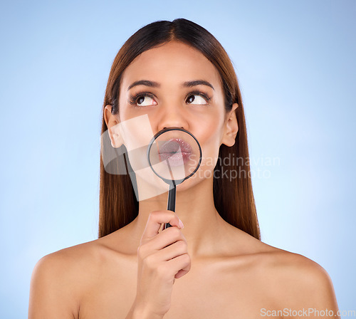 Image of Pouting, skincare and a woman with a magnifying glass on mouth isolated on a blue background. Goofy, thinking and a girl with a tool for a closeup on lips, beauty and cosmetics on a backdrop