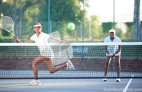 Image of Tennis, fitness and a sports woman hitting a ball over a net during a competitive game to return a serve. Exercise, health or training with a female athlete and doubles partner playing on a court