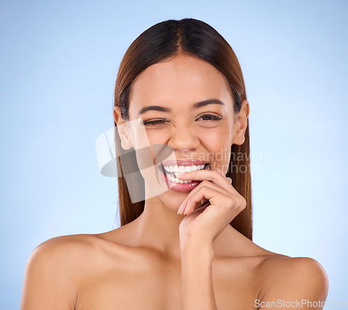 Image of Beauty, woman and biting finger and wink portrait for skincare dermatology cosmetics in studio. Female model person on blue background for self care, facial glow and healthy or clean skin with smile