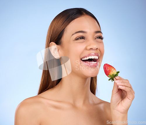 Image of Skincare, wellness and woman with a strawberry in studio with a healthy, natural and face routine. Happy, beauty and female model with dermatology facial treatment eating red fruit by blue background