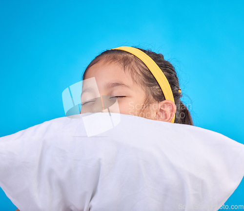 Image of Little girl, pillow and sleep in a studio feeling tired, fatigue and ready for dreaming. Isolated, blue background and happy young child with pillows and closed eyes for sleeping, rest and nap