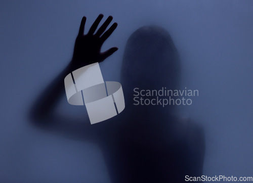 Image of Shadow, glass and hand with a woman in studio on a blue background for mystery or sensual secrecy. Creative, silhouette and window with a female posing for beauty, art deco or feminine desire