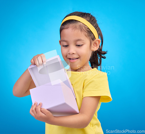 Image of Box, surprise and child with gift in studio on blue background for present, birthday or celebration. Happiness, smile and isolated young, excited and happy girl opening package, product and parcel