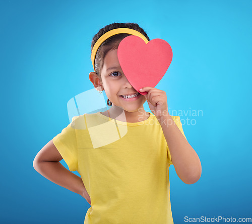 Image of Portrait, heart cut out and girl with smile, joyful and cheerful against blue studio background. Face, female kid and young person with symbol for love, happiness and joyful with development and sign