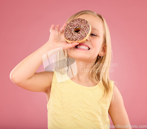 Image of Child, donut and smile portrait in studio on a pink background while happy about sweet snack. Girl kid model with happiness, creativity and chocolate ring over eye in hand isolated on color and space