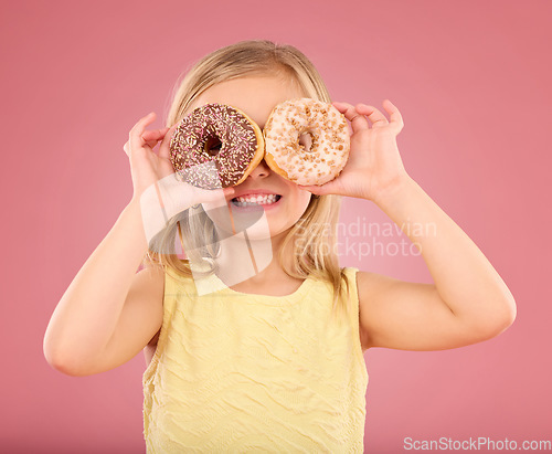 Image of Child, donut over eyes and smile in studio with sweet snack in hands on a pink background. Girl kid model with happiness, creativity and comic face holding food in hand isolated on color and space