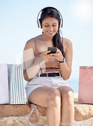 Image of Woman relax after shopping, smartphone and headphones, listening to music outdoor with retail therapy and rest. Happy female, paper bag and communication with chat on social media app and technology