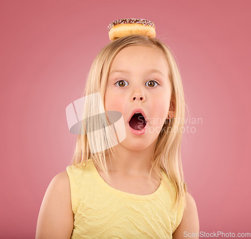 Image of Child, wow and donut portrait in studio with surprise on head on a pink background. Face of a girl kid model with mouth open, shocked and comic chocolate snack isolated on creative color and space