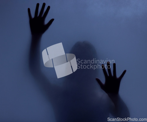 Image of Horror, mystery and shadow of a woman on a window for fear, escape or nightmare. Dark, hands and a ghost, girl or person with paranormal activity, spooky behavior or strange movement in a studio