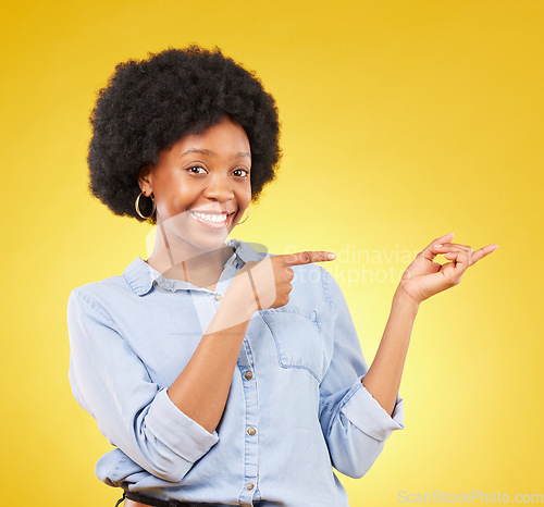 Image of Happy, portrait of a black woman in studio pointing at mockup space for advertising or marketing. Happiness, smile and African female model showing mock up for product placement by yellow background.