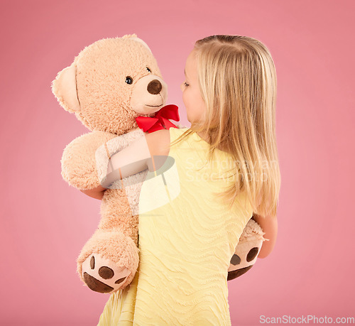 Image of Teddy bear, happy and back of a child in studio with a big, fluffy and cute toy as gift or present. Adorable, innocent and young girl kid hugging her teddy with care and happiness by pink background.