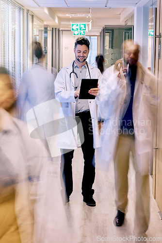 Image of Digital tablet, happy and man doctor walking in a busy hospital, excited while checking online schedule. Motion blur, male and healthcare expert with app for planning, communication and prescription