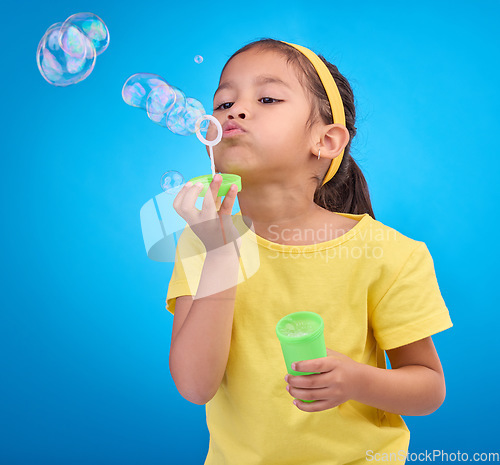 Image of Children, blue background and a girl blowing bubbles in studio for fun or child development of motor skills. Kids, game or soap and a cute or adorable female child playing with a bubble wand