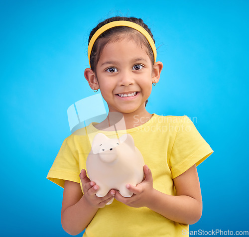 Image of Face portrait, piggy bank and girl child in studio isolated on a blue background. Happy, smile and kid with cash box, savings or financial, investment or learning budget, finance growth or money.