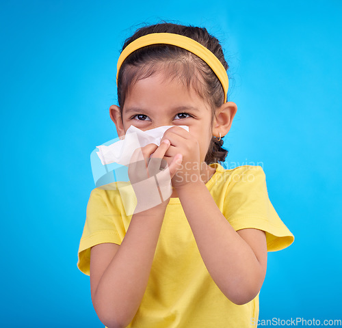 Image of Sick, blowing nose and napkin with girl in studio for allergies, illness and sneezing. Hay fever, bacteria and sinus issue with child and tissue isolated on blue background for health, medical or flu