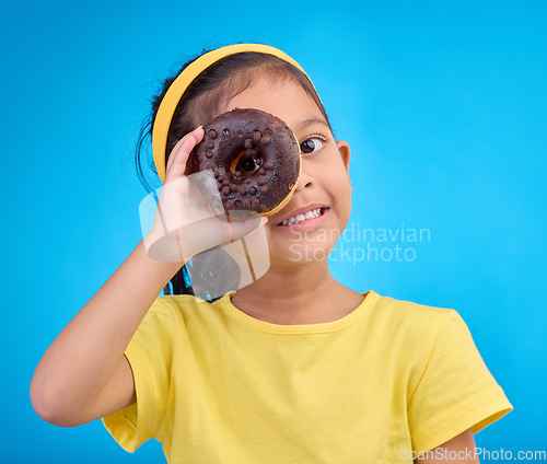 Image of Donut, eye and smile with portrait of girl in studio for junk food, sugar and happiness. Snack, cake and cute with face of child and dessert for cute, positive and chocolate on blue background