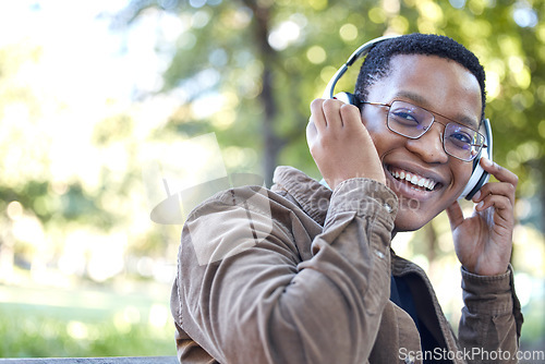 Image of Headphones, park and portrait of african man listening to music for outdoor, mental health and relaxing break in nature. Young, happy student or black person with audio technology in garden or campus
