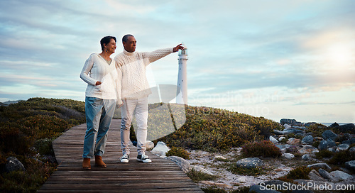 Image of Travel, love and elderly couple pointing on boardwalk at beach, calm at a lighthouse against sunset sky. Senior, man with woman on ocean trip, holiday or vacation, happy and enjoying retirement