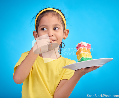 Image of Birthday cake, taste and young girl with a sweet in studio eating icing for party event dessert. Celebration, rainbow food and hungry kid in a isolated and blue background studio ready to celebrate