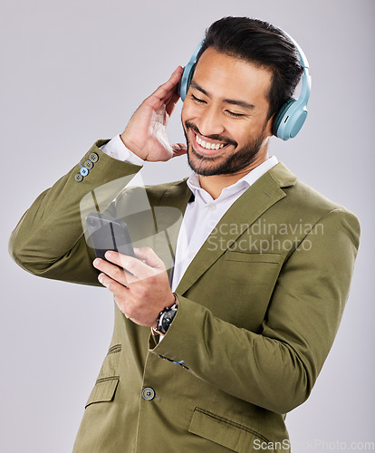 Image of Asian man, phone and smile listening to music on headphones against a gray studio background. Happy formal male smiling on smartphone with headset for audio streaming or entertainment on mobile app