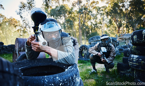 Image of Team, paintball and tires for cover, hiding or protection while firing or aiming down sights together in nature. Group of paintballers waiting in teamwork for opportunity to attack or shoot in sports