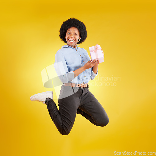 Image of Jump, excited and black woman with gift in air on yellow background with energy, happy and smile in studio. Birthday mockup, celebrate and isolated girl jumping with present, box and surprise package