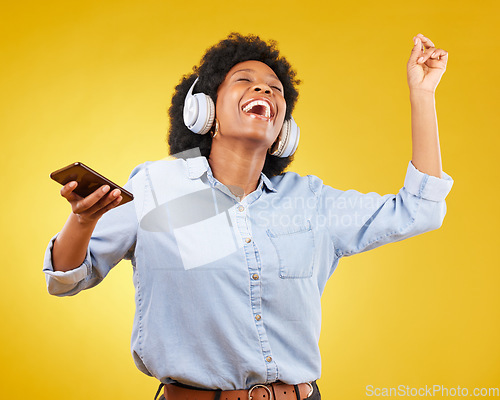 Image of Phone, music headphones and black woman singing in studio isolated on a yellow background. Dance, cellphone and happy female with mobile for streaming, dancing and enjoying radio, podcast or audio.