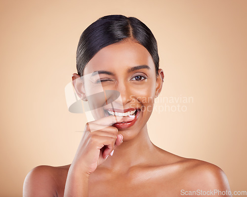 Image of Flirty, beauty and portrait of a winking woman isolated on a studio background. Happy, sexy and face of an Indian model with makeup, cosmetics and attitude on a backdrop to advertise lipstick